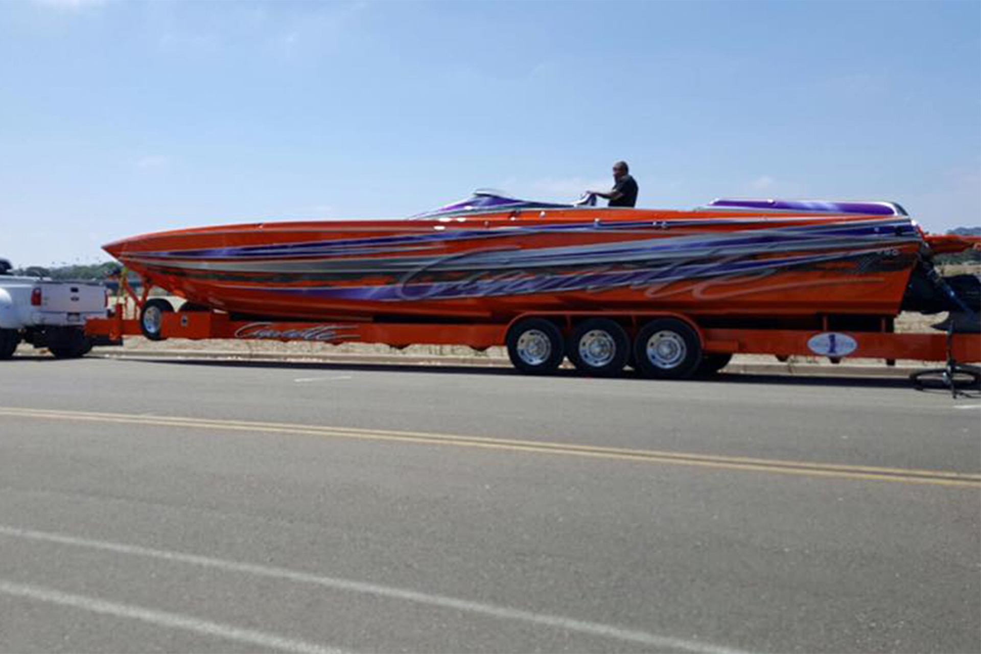 Custom cigarette boat on trailer being pulled by a pickup truck.